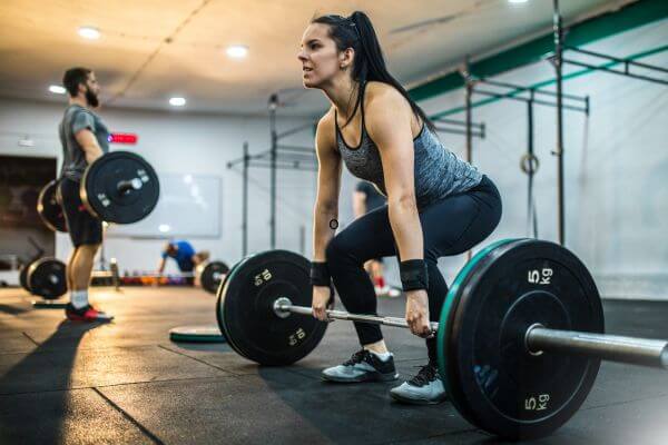 Mulher em academia fazendo exercícios com grandes pesos. 