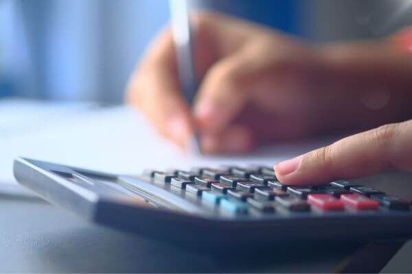 Cálculo de parcelamento para negociação de débitos federais Pessoa realizando cálculos em calculadora para avaliar parcelamento e descontos na transação tributária de débitos federais